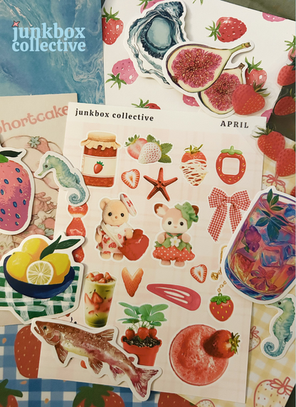 Collection of colorful stickers that are fruity, marine life, and strawberry picks with various designs on a variety of checked blue scrap paper surface, featuring the 'junkbox collective' custom sticker sheets
